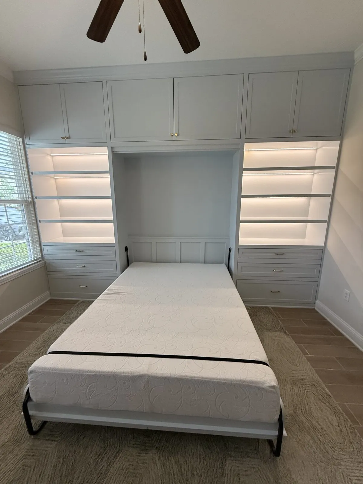 Custom Murphy bed lowered between lighted shelving towers
