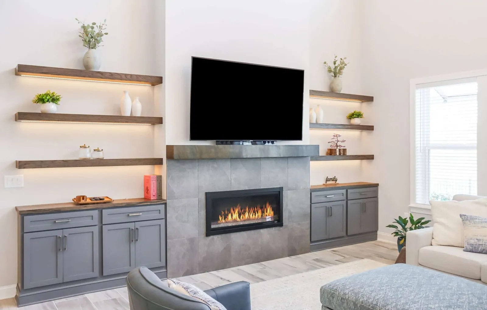 Lighted wood floating shelves on both sides of a TV and tiled fireplace
