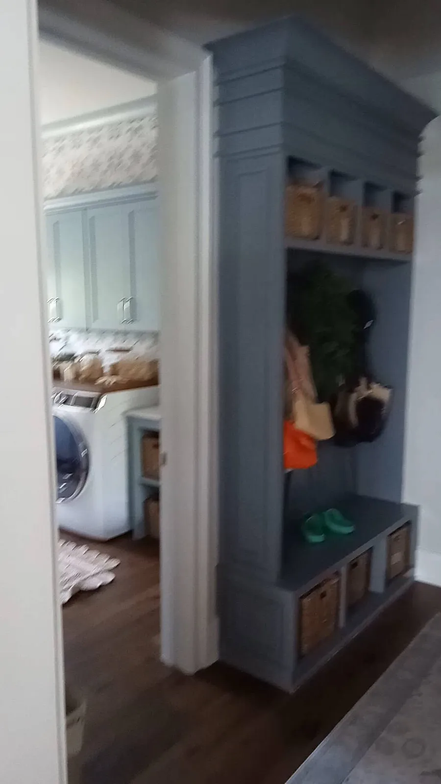 Blue-gray mudroom locker with cubbies, hooks and a bench beside a laundry room