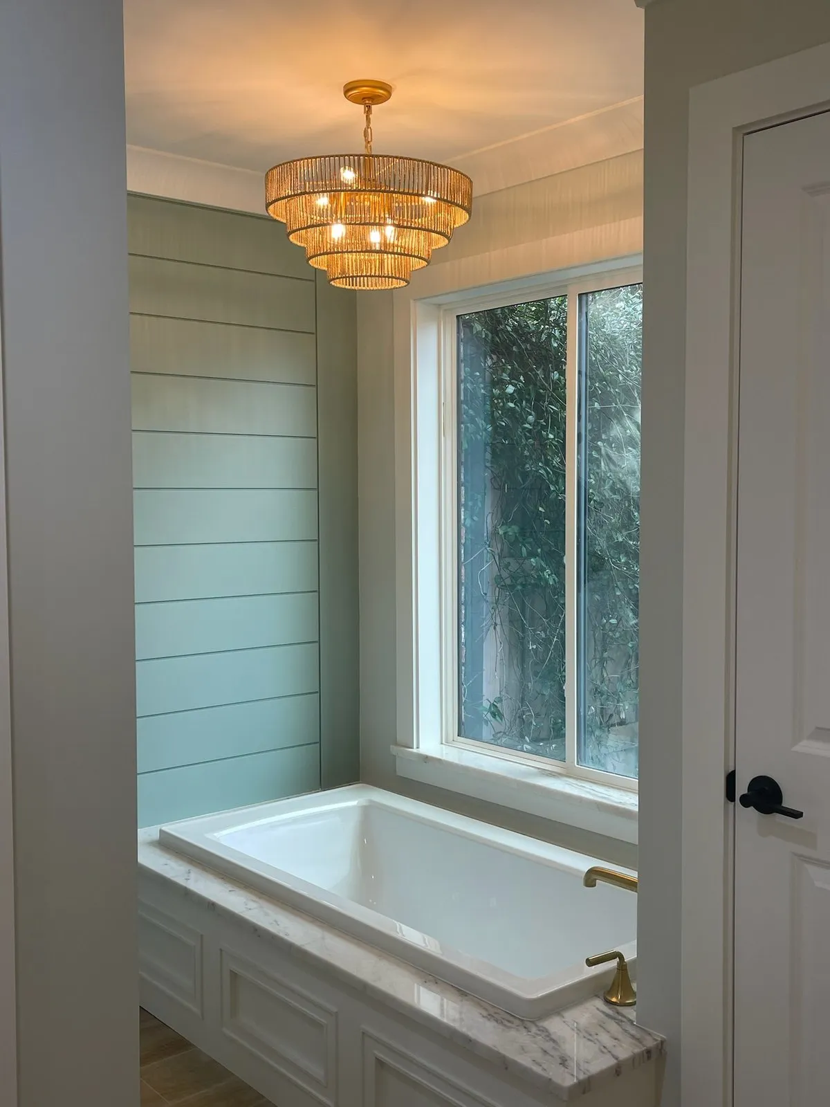 Painted shiplap accent wall behind a soaking tub under a chandelier